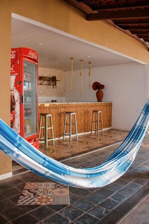 A room with a red Coca-Cola refrigerator, a bamboo bar counter, and a hammock.