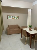 Una habitación con un sofá color beige, una mesa de comedor con sillas y una planta en maceta.