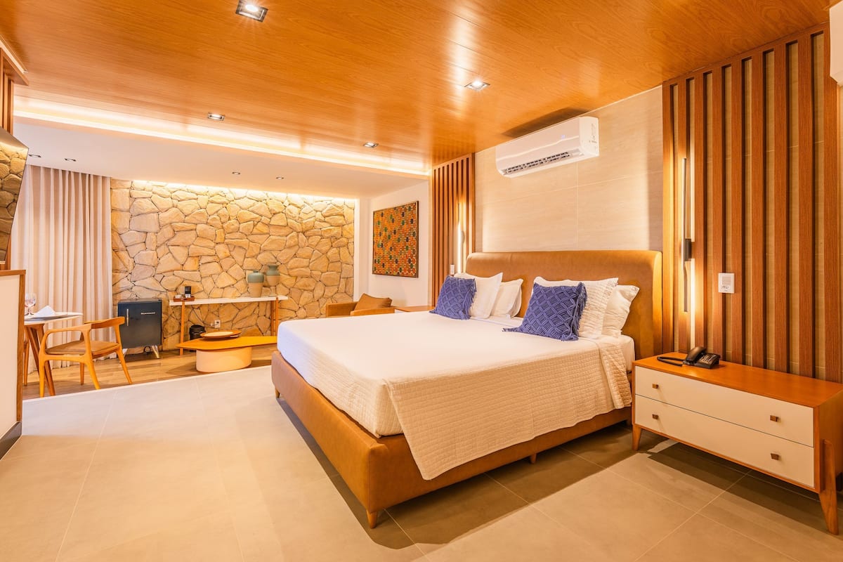 A modern bedroom with a large bed, bedside tables, a desk, and a stone wall.