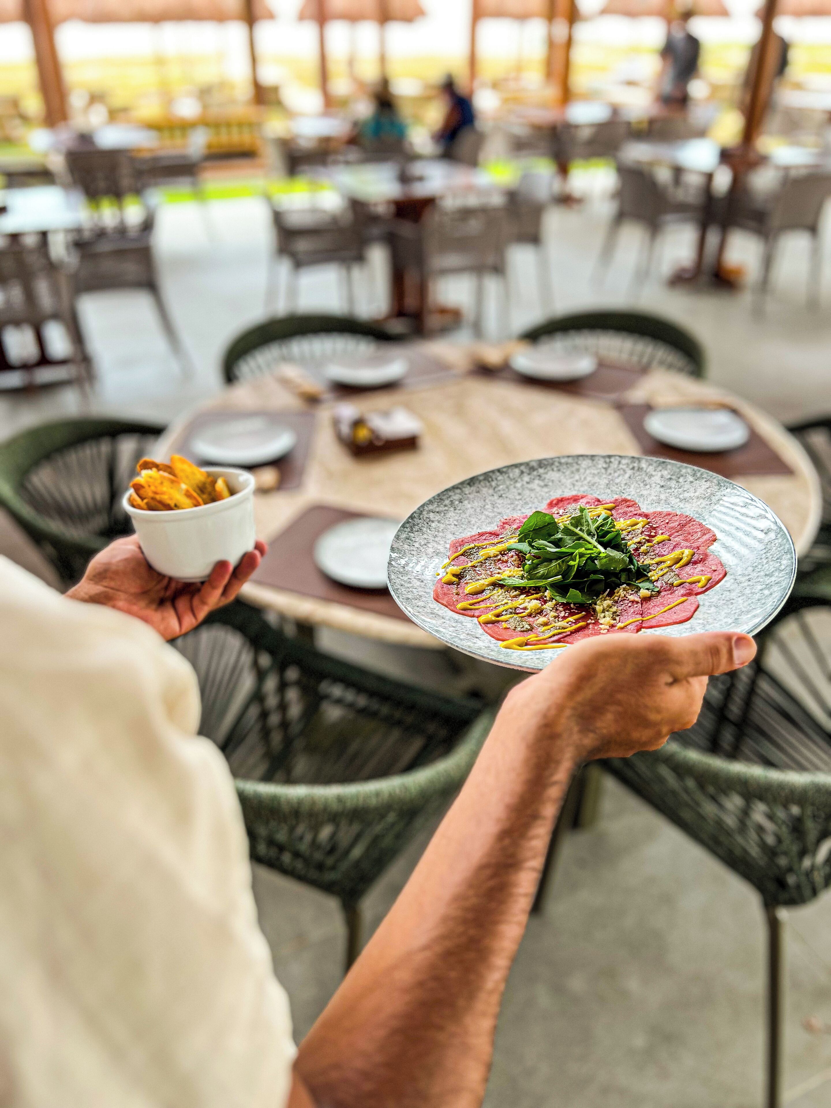A person holding a plate with a meal and a small bowl of chips.