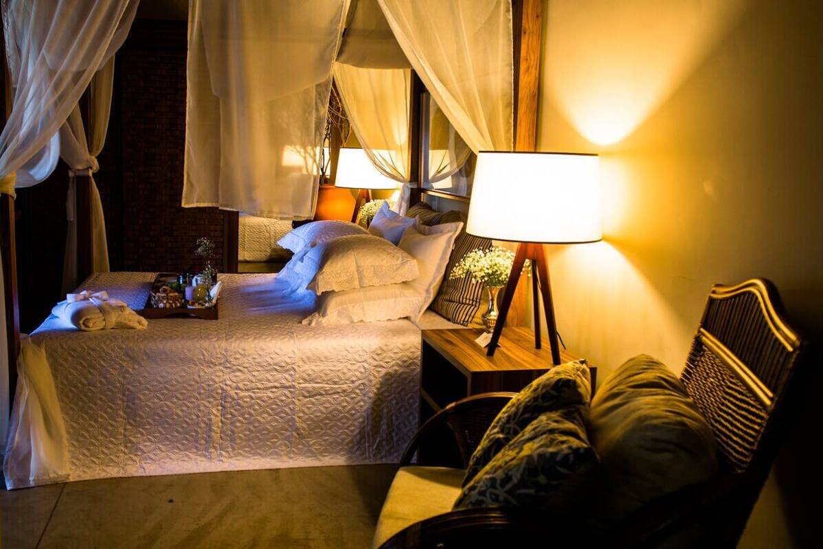 A bed with a canopy, bedside lamps, a bedside table with a vase, and a chair.