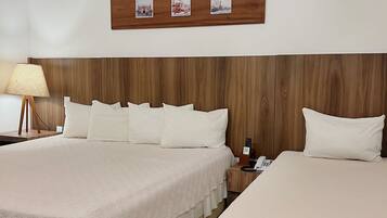 Habitación de hotel con dos camas, cabecero de madera, mesita de noche con lámpara y un cuadro colgado en la pared.