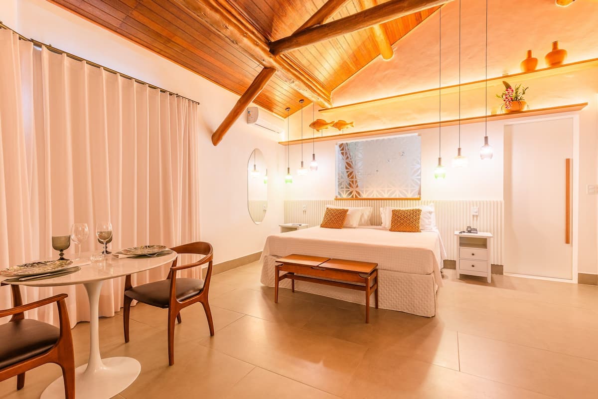 A modern hotel room with a bed, bedside table, and a dining area with a table and chairs.