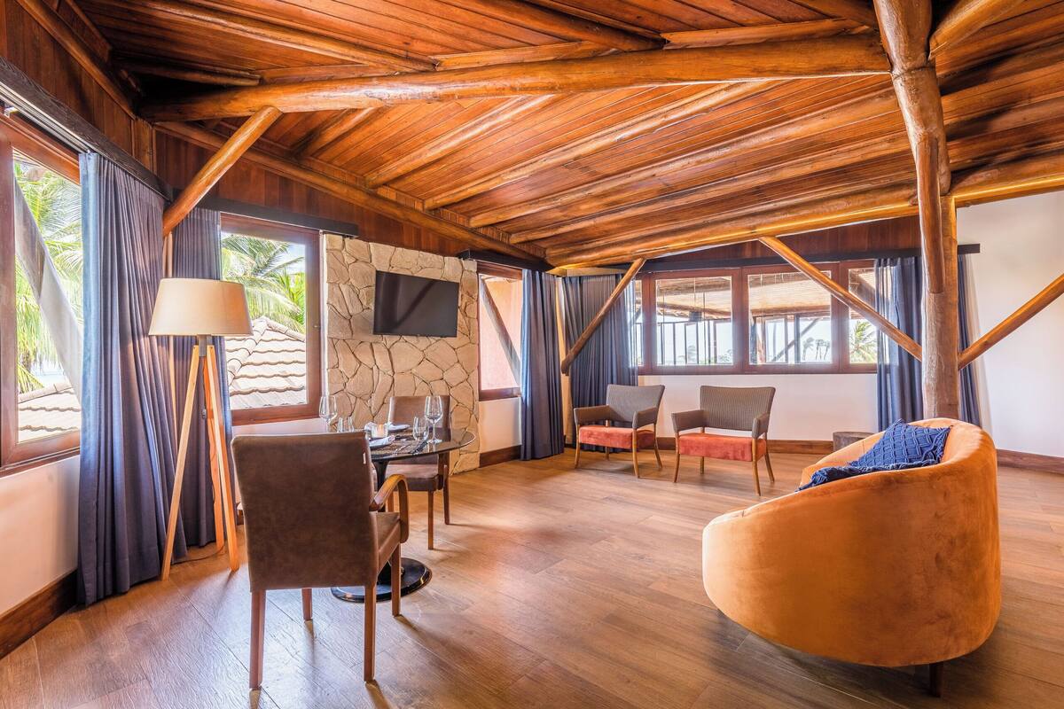A spacious room with a wooden ceiling, a stone wall, a flat-screen TV, and a dining area with chairs and a table.