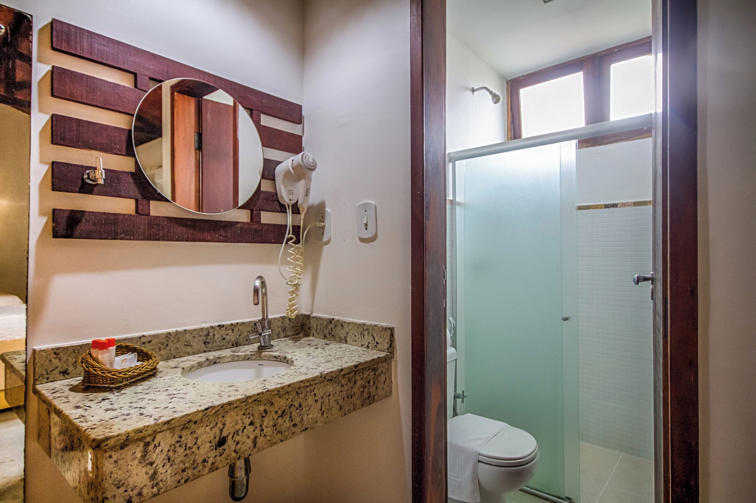 A bathroom with a granite countertop, a round mirror, a hairdryer, and a toilet.