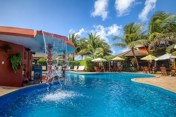 Relax by the pool surrounded by lounge chairs and umbrellas, with a soothing water feature nearby.