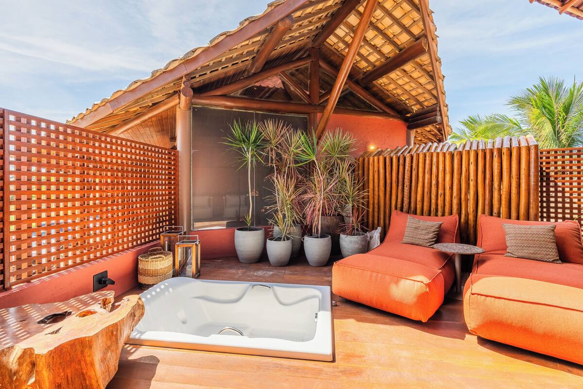 A sunlit outdoor seating area with a wooden deck, a hot tub, and potted plants.