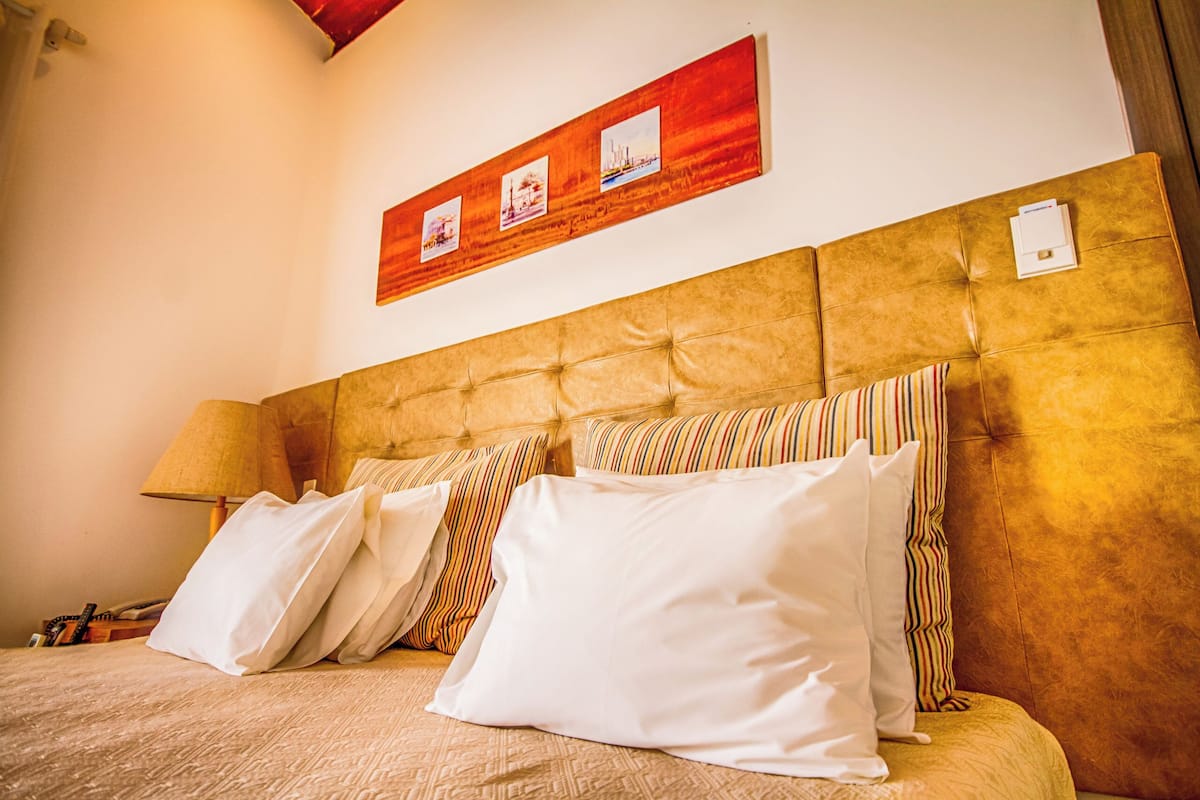 A hotel room with a large bed, multiple pillows, a headboard, a lamp, and a wall-mounted picture.