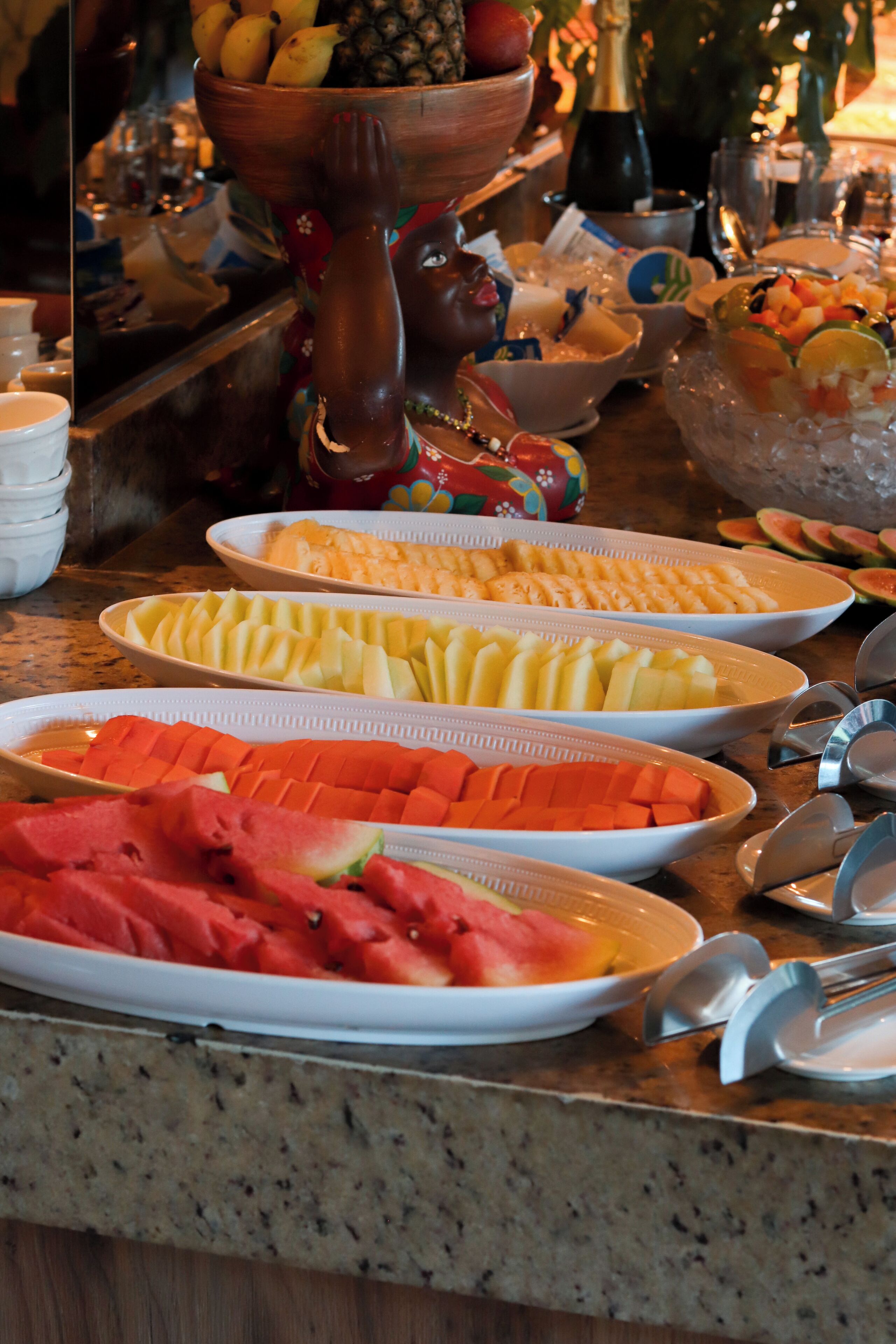 A buffet table with various fruits and a bottle of champagne.