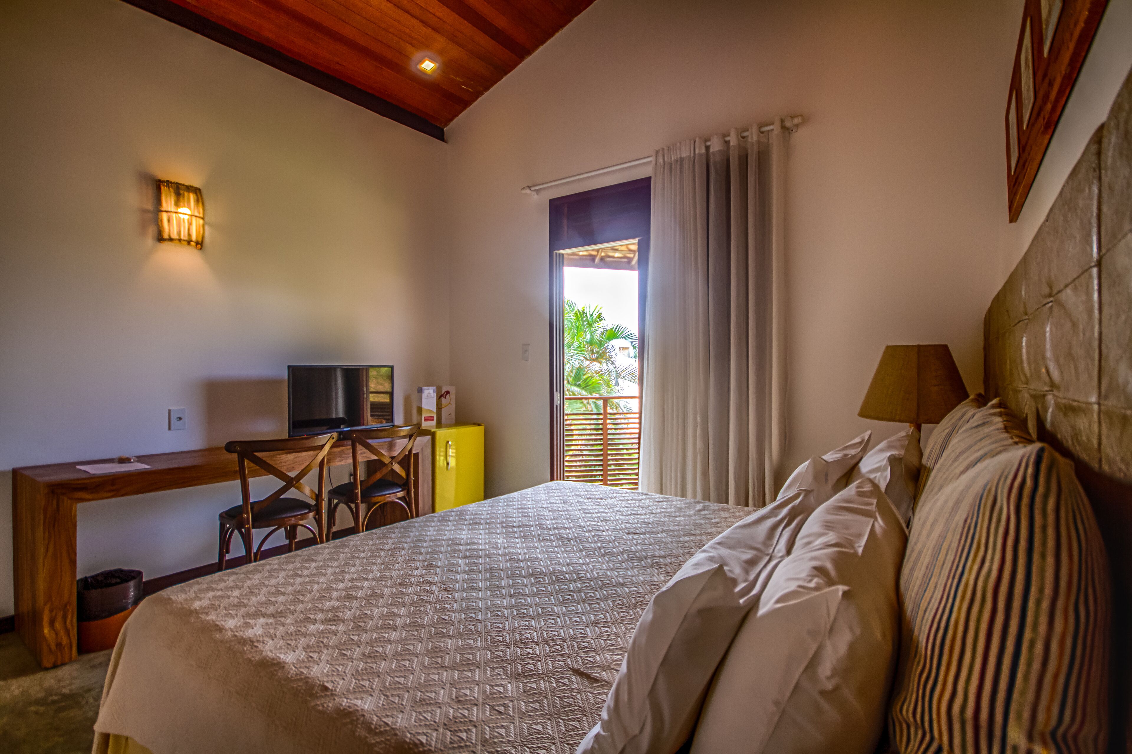 A hotel room with a bed, a desk with a television, a chair, and a window with curtains.