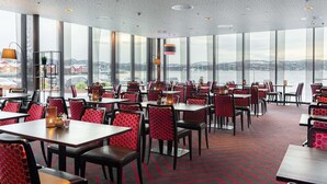 A restaurant with multiple tables and chairs, large windows, and a view of a snowy landscape. - Scandic Rock City (Namsos)