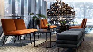 A modern lounge area with orange upholstered chairs, a black coffee table, and a grey ottoman. A potted plant is on the table, and a unique wooden wall art piece is in the background. - Scandic Rock City (Namsos)