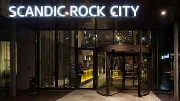 Der Eingang von Scandic Rock City mit Glasfassade, einer Drehtür und einem sichtbaren Innenraum mit gelben Akzenten.