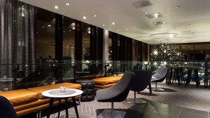 A modern lounge area with leather seating, a round table, and a decorative light fixture. - Scandic Rock City (Namsos)