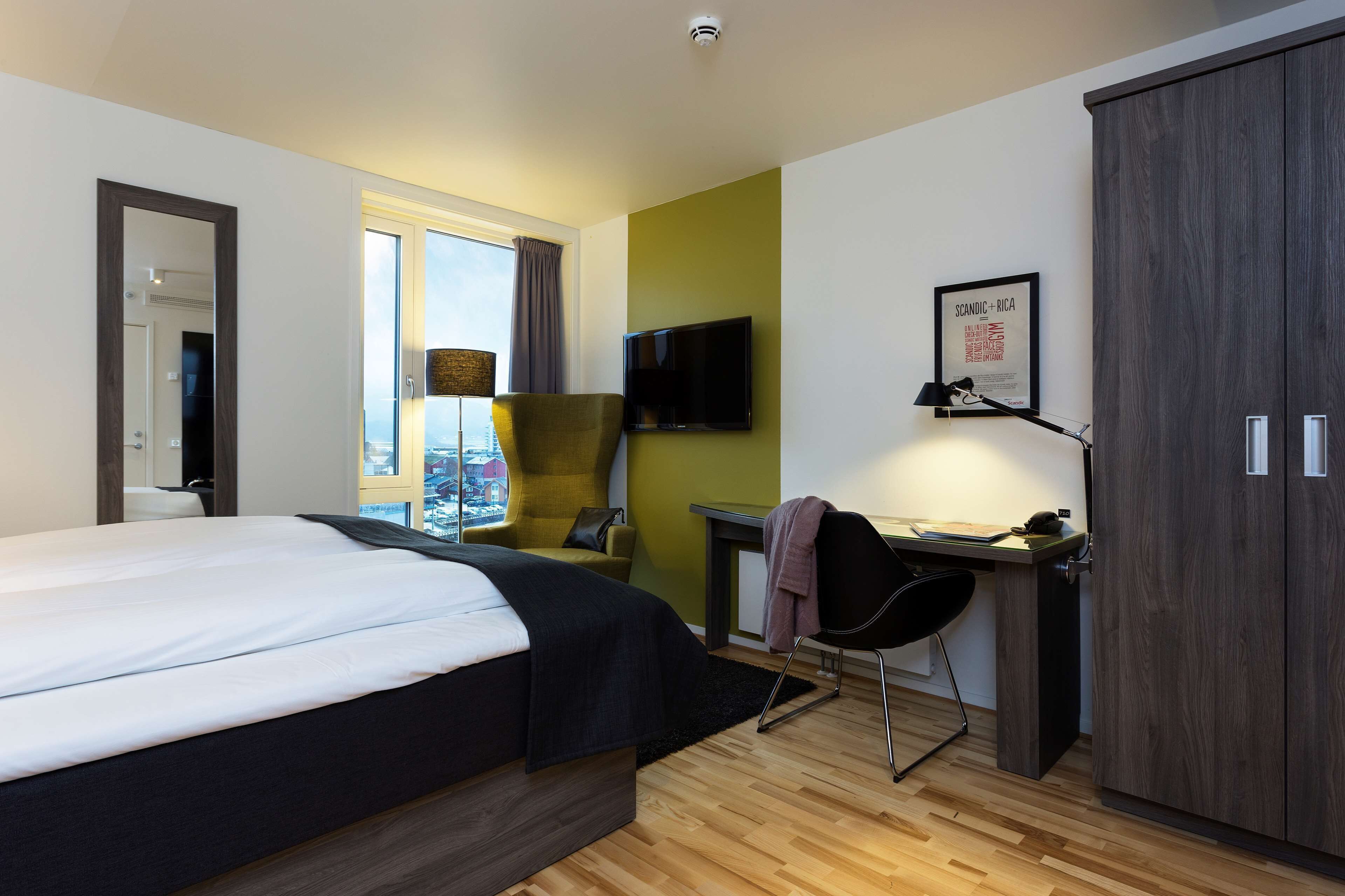 Une chambre d’hôtel moderne avec un grand lit, un bureau équipé d’un ordinateur, une chaise et une armoire.