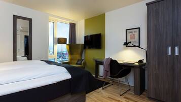 Une chambre d’hôtel moderne avec un grand lit, un bureau équipé d’un ordinateur, une chaise et une armoire.