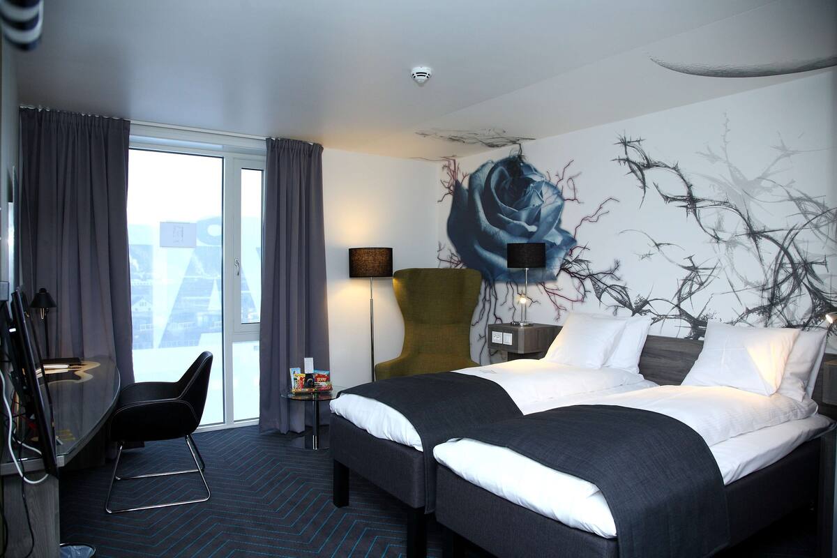 A hotel room with a bed, a desk, a chair, and a large window.