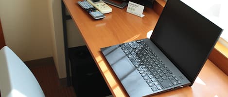 A laptop on a wooden desk with a remote control and a sign.