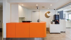A reception area with a bright orange counter, a Dell computer, and a coffee machine. - Comfort Inn Suwa Inter (Suwa)