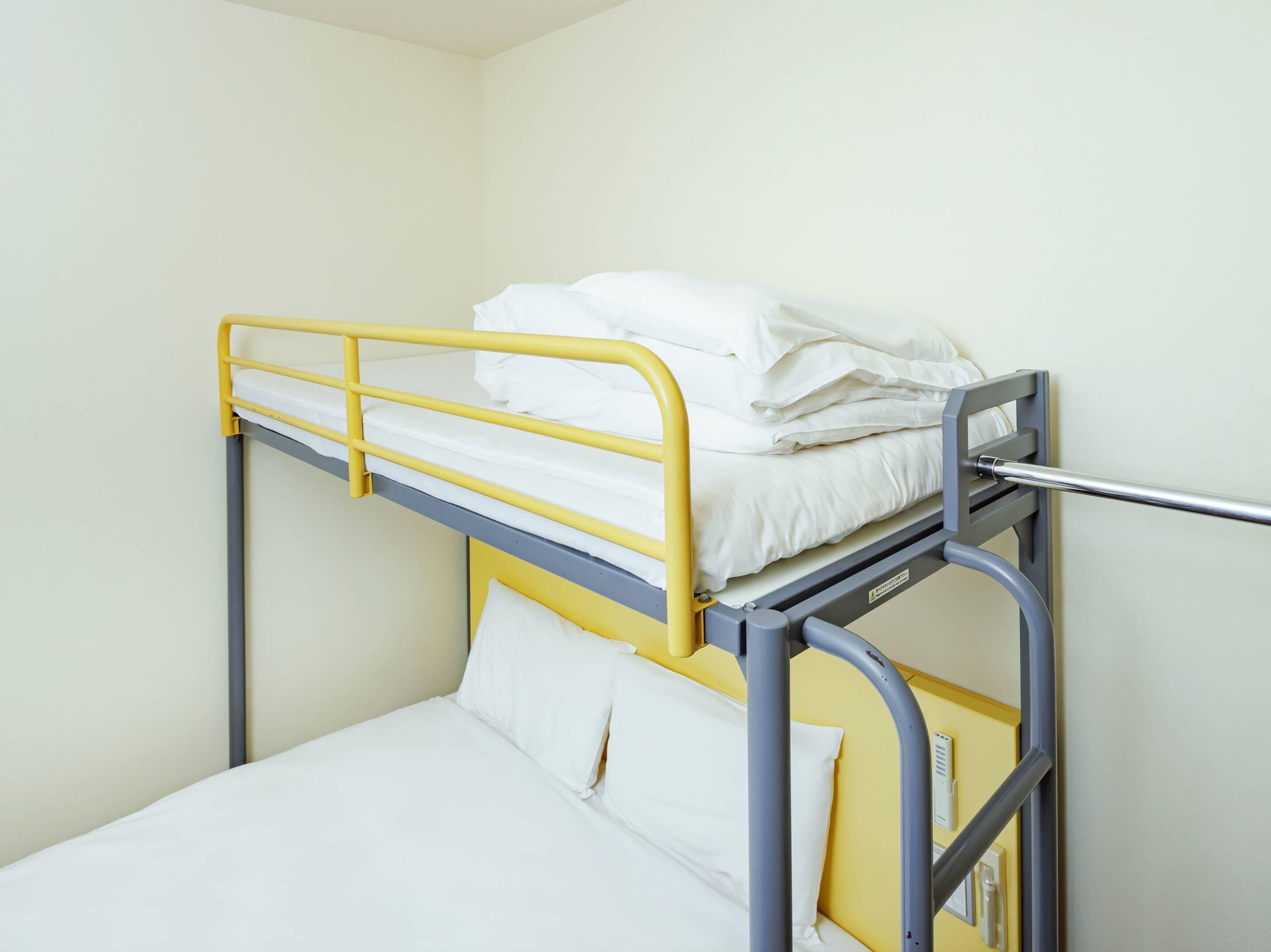 A bunk bed with a yellow frame and white bedding.