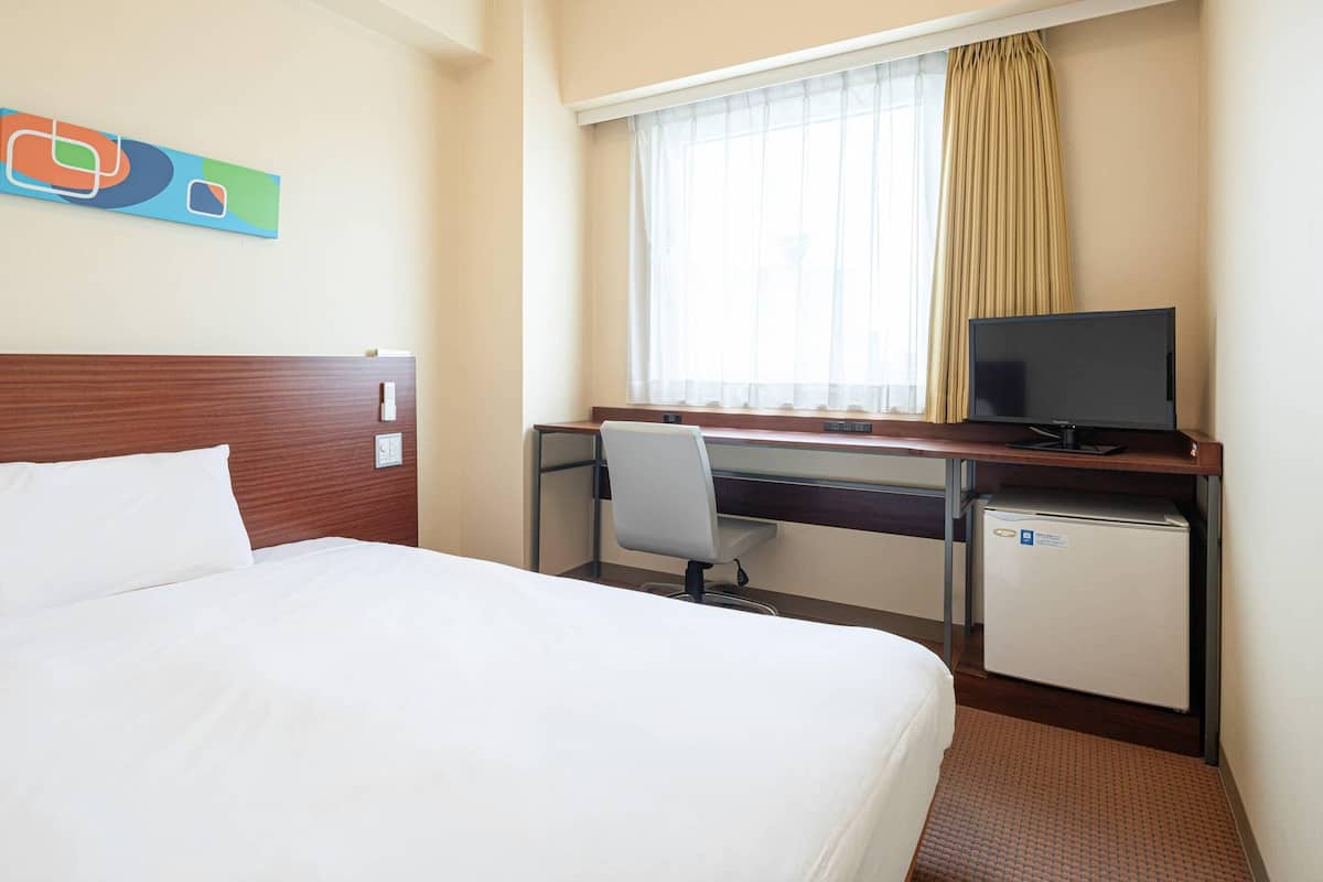 A hotel room with a bed, a desk with a computer, a television, and a small refrigerator.