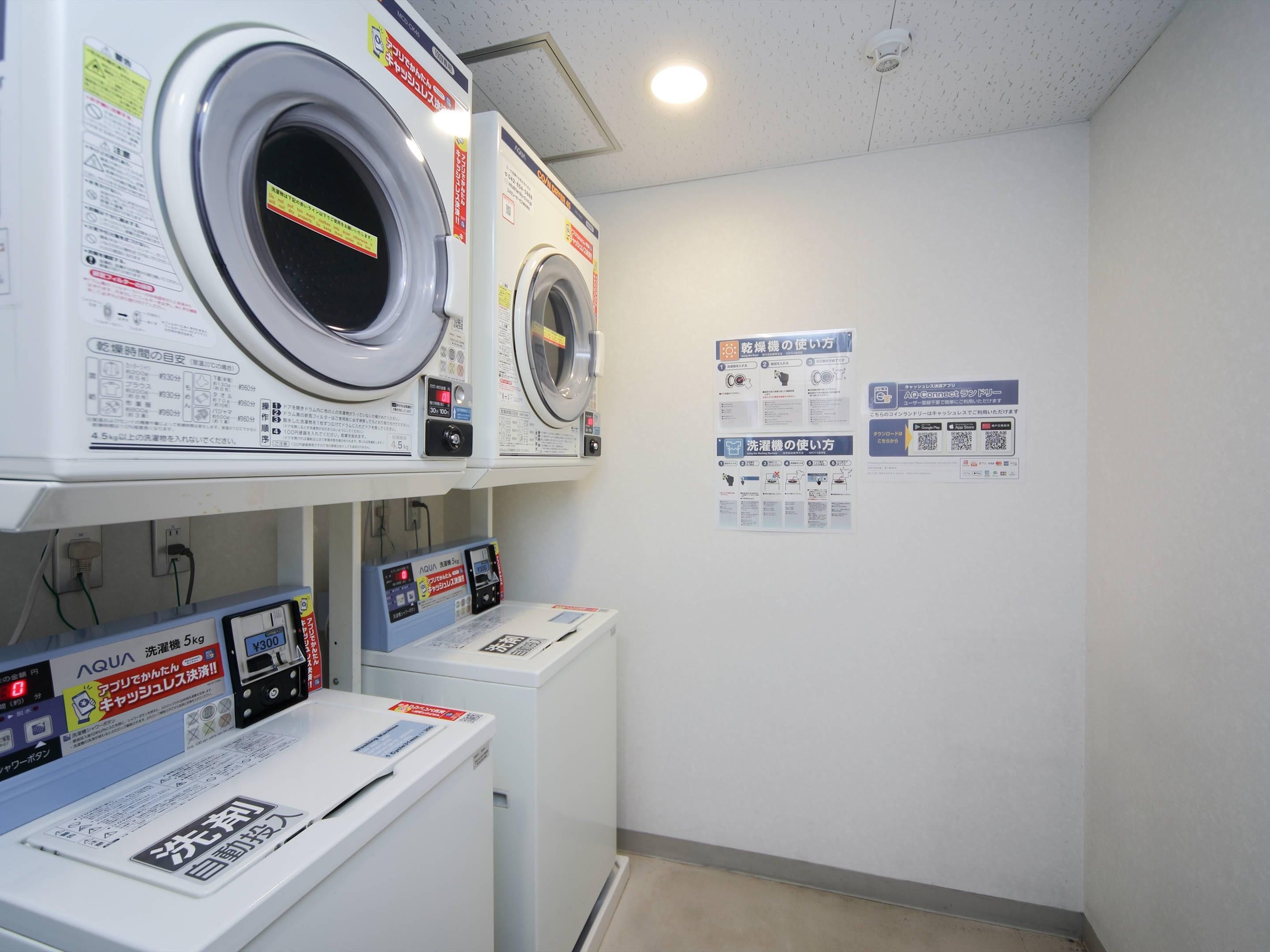 Un espace buanderie équipé de deux machines à laver et d’un sèche-linge, chacun étant accompagné d’affiches explicatives accrochées au mur.