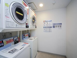 Un área de lavandería con dos lavadoras y una secadora, cada una con carteles informativos en la pared.