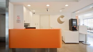 Zona de recepción con un mostrador naranja brillante, un quiosco digital y un cartel que indica sala privada.