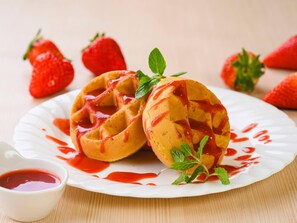 A plate with two waffles topped with red syrup and mint leaves, accompanied by a small bowl of syrup and fresh strawberries in the background. - Comfort Inn Munakata (Munakata)