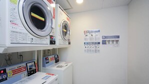 Un área de lavandería con dos lavadoras y una secadora, cada una con carteles informativos en la pared.