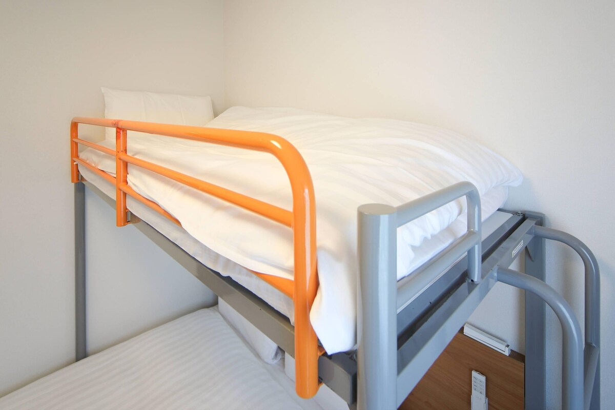 A bunk bed with an orange frame and white bedding.