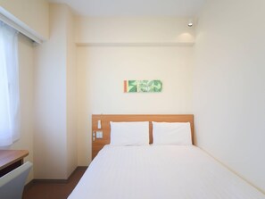 A hotel room with a bed, a wooden headboard, a small table, and a wall-mounted light fixture.