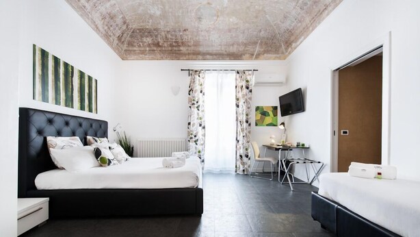 Una habitación de hotel con una cama grande, una cama más pequeña, un escritorio con silla y un televisor montado en la pared.