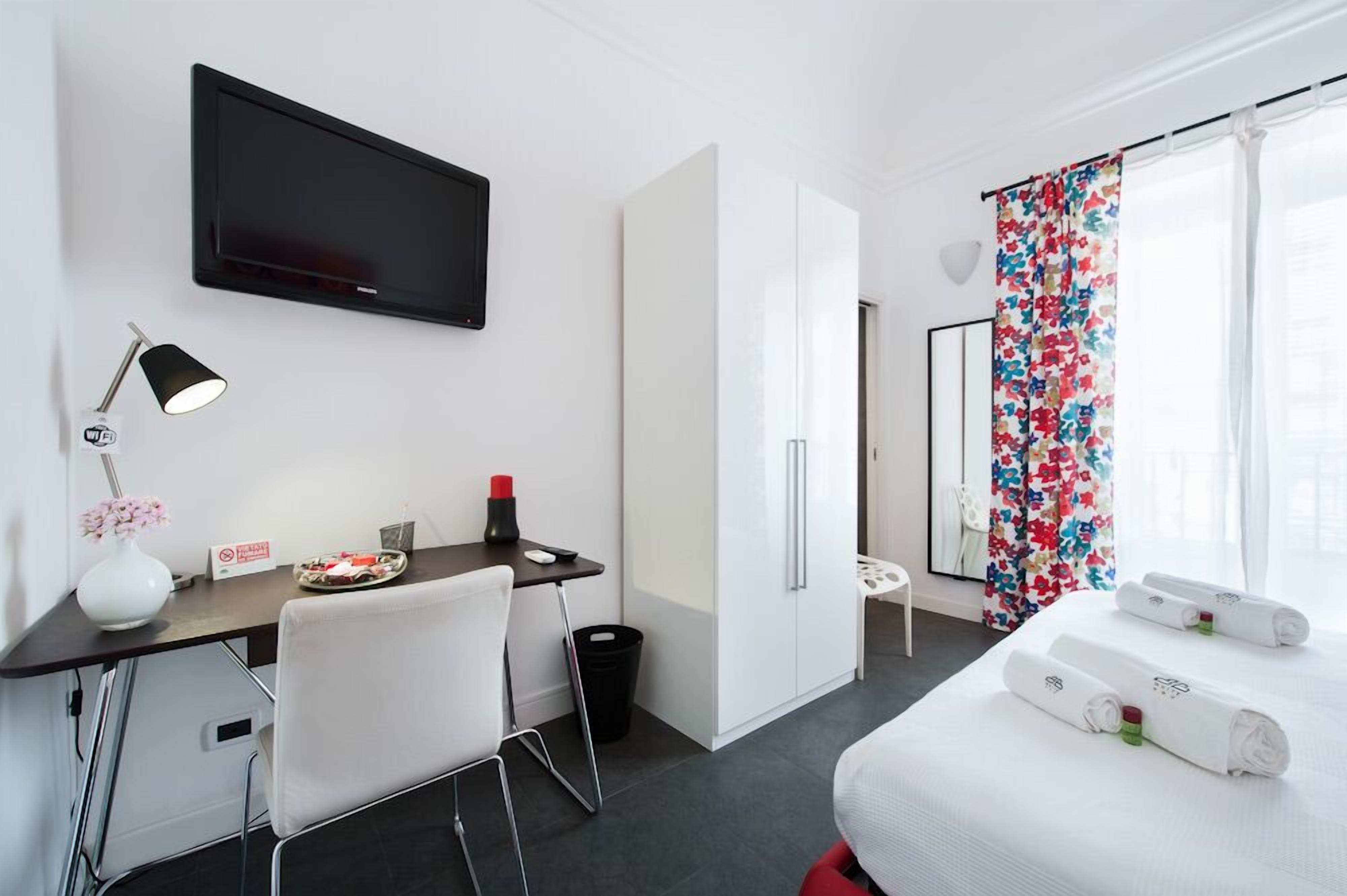 A hotel room with a bed, a desk with a chair, a TV, and a window with curtains.