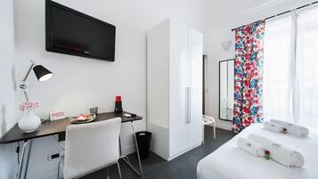 A hotel room with a bed, a desk with a chair, a TV, and a window with curtains.