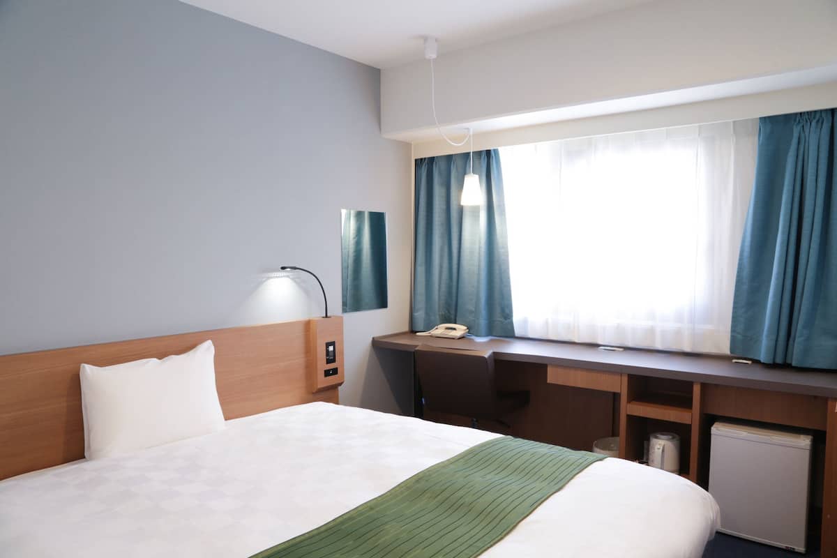 A hotel room with a bed, desk, and a small refrigerator.