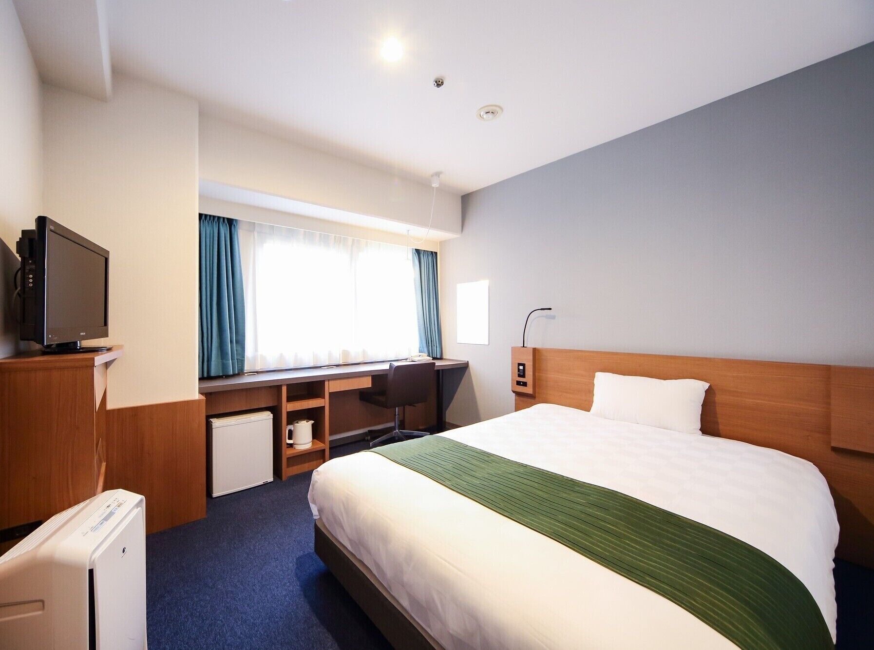 A hotel room with a bed, a desk, a television, and a window with curtains.