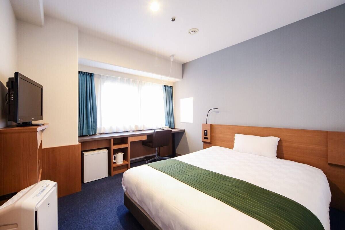 A hotel room with a bed, a desk, a television, and a window with curtains.