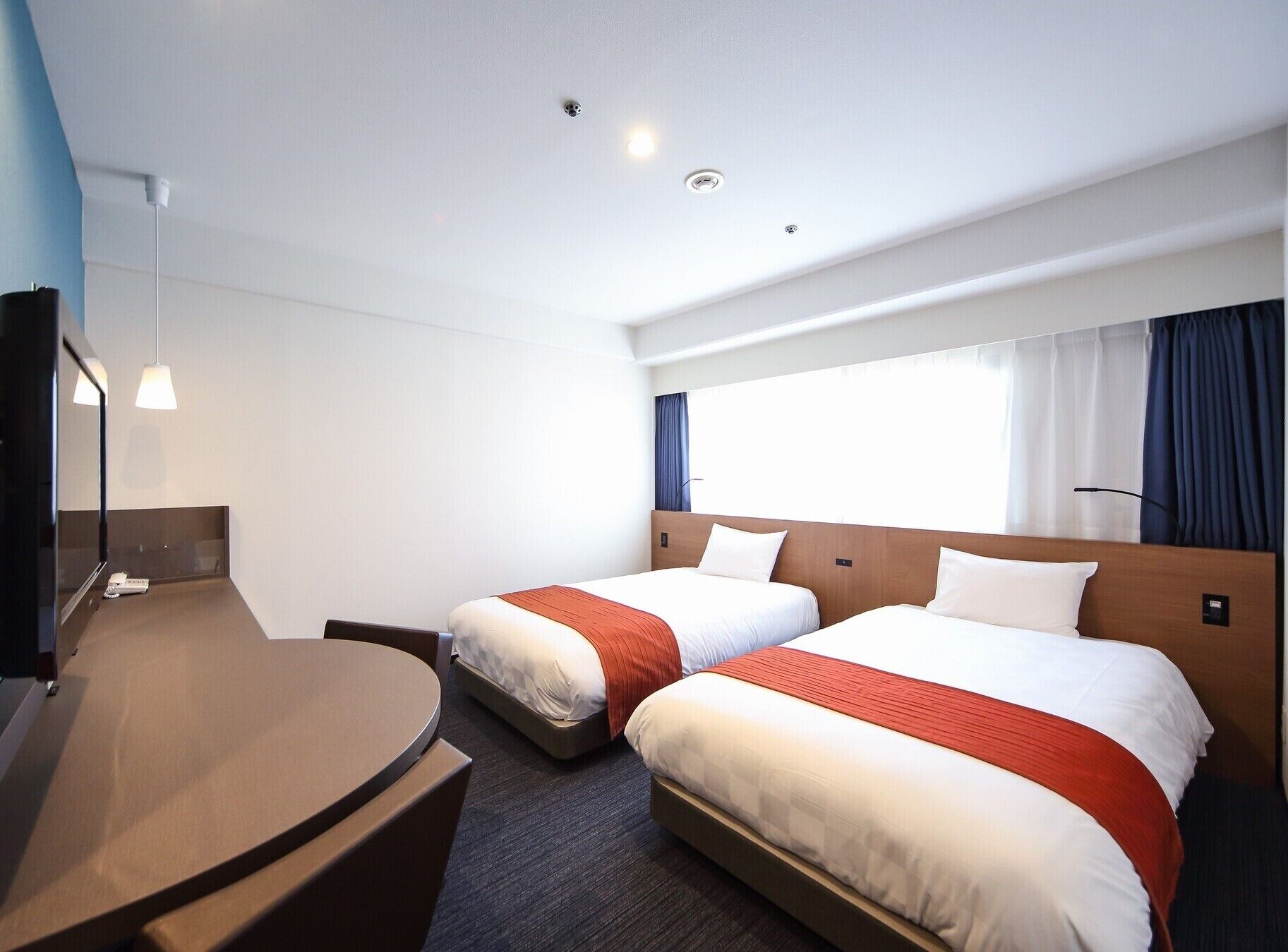 A hotel room with two beds, a desk, a mirror, and a window with curtains.