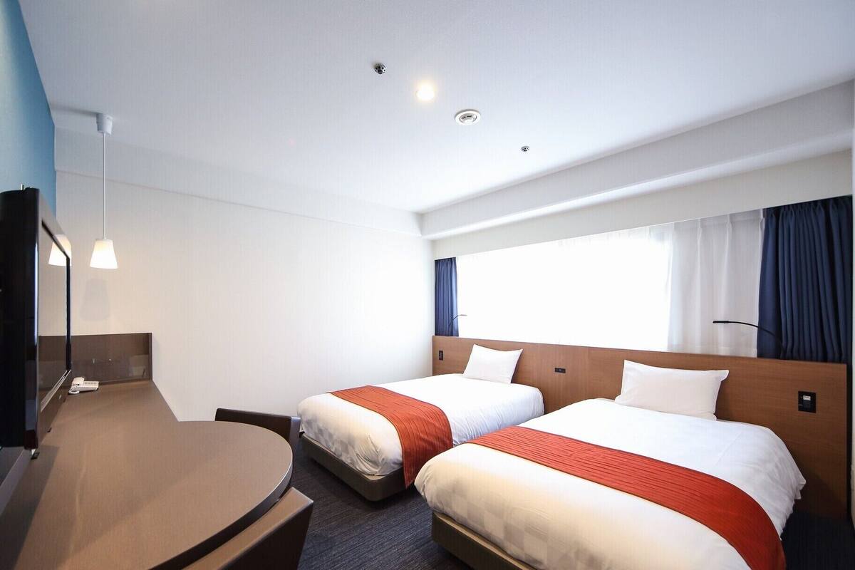 A hotel room with two beds, a desk, a mirror, and a window with curtains.