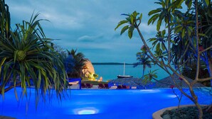 Una piscina infinita con vistas al mar, rodeada de plantas tropicales y sillones de descanso.