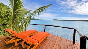 Una terraza de madera con dos sillones naranjas mirando a un lago tranquilo, rodeada de vegetación.