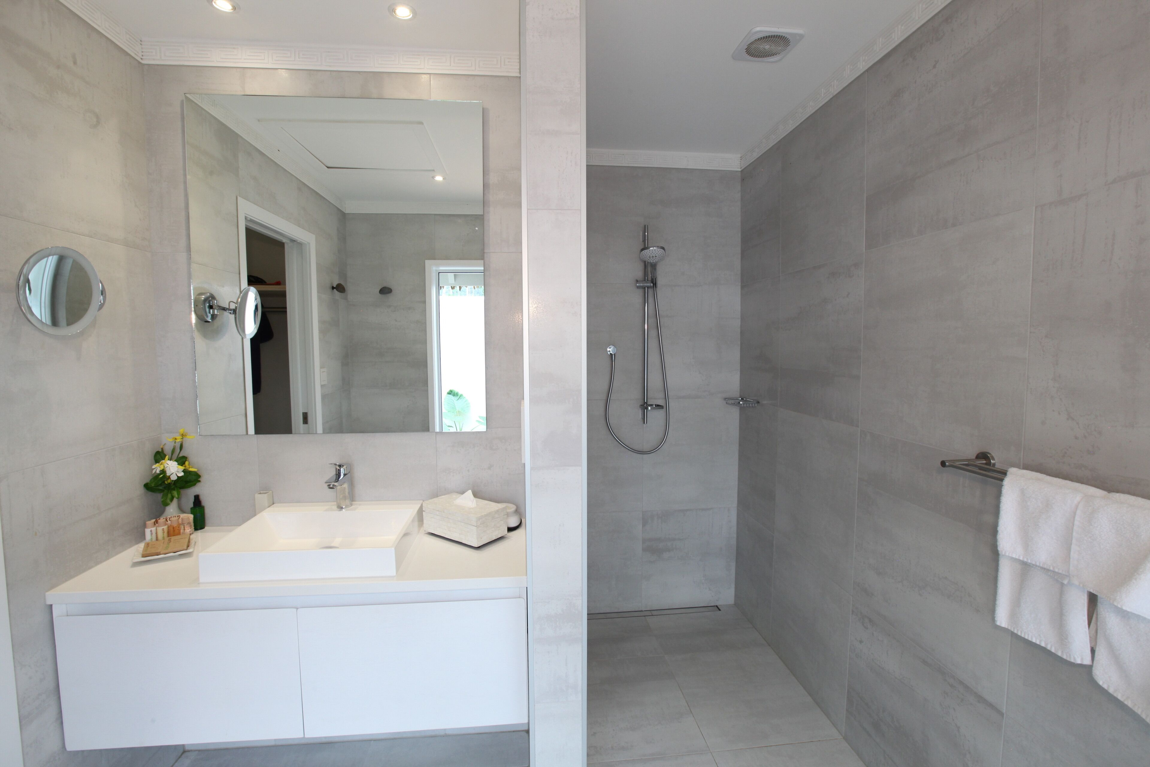 A modern bathroom with a large mirror, a white sink, and a shower area.