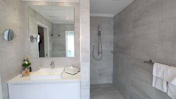 A modern bathroom with a large mirror, a white sink, and a shower area.