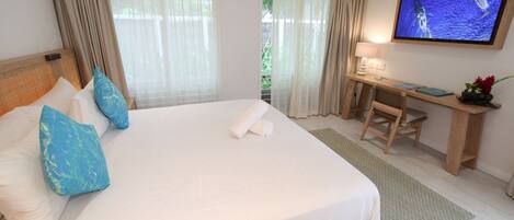 A hotel room with a large bed, a desk, a television, and a view of greenery outside.