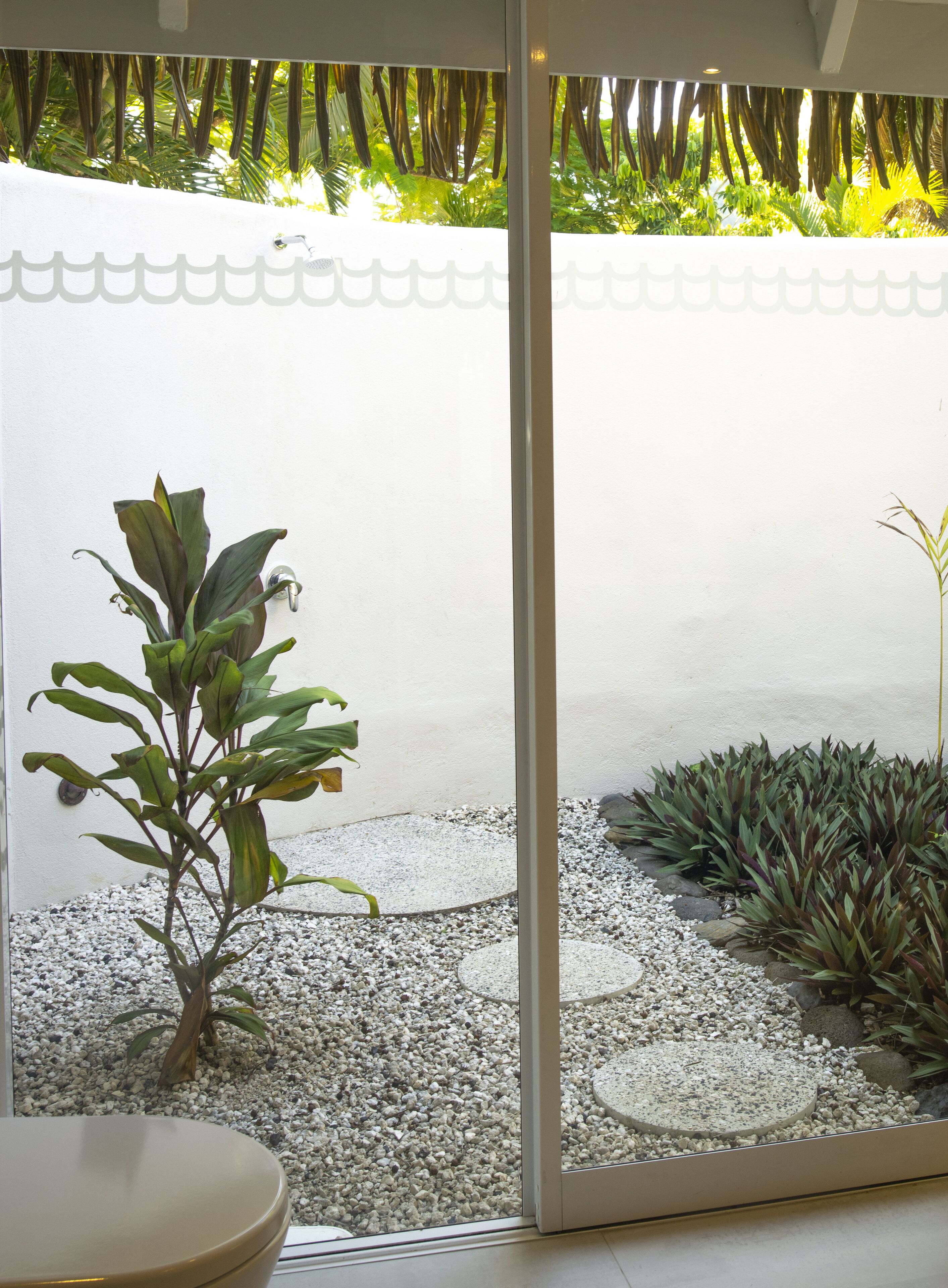 A view through a glass door of a patio area with a small plant, pebbles, and a white wall.