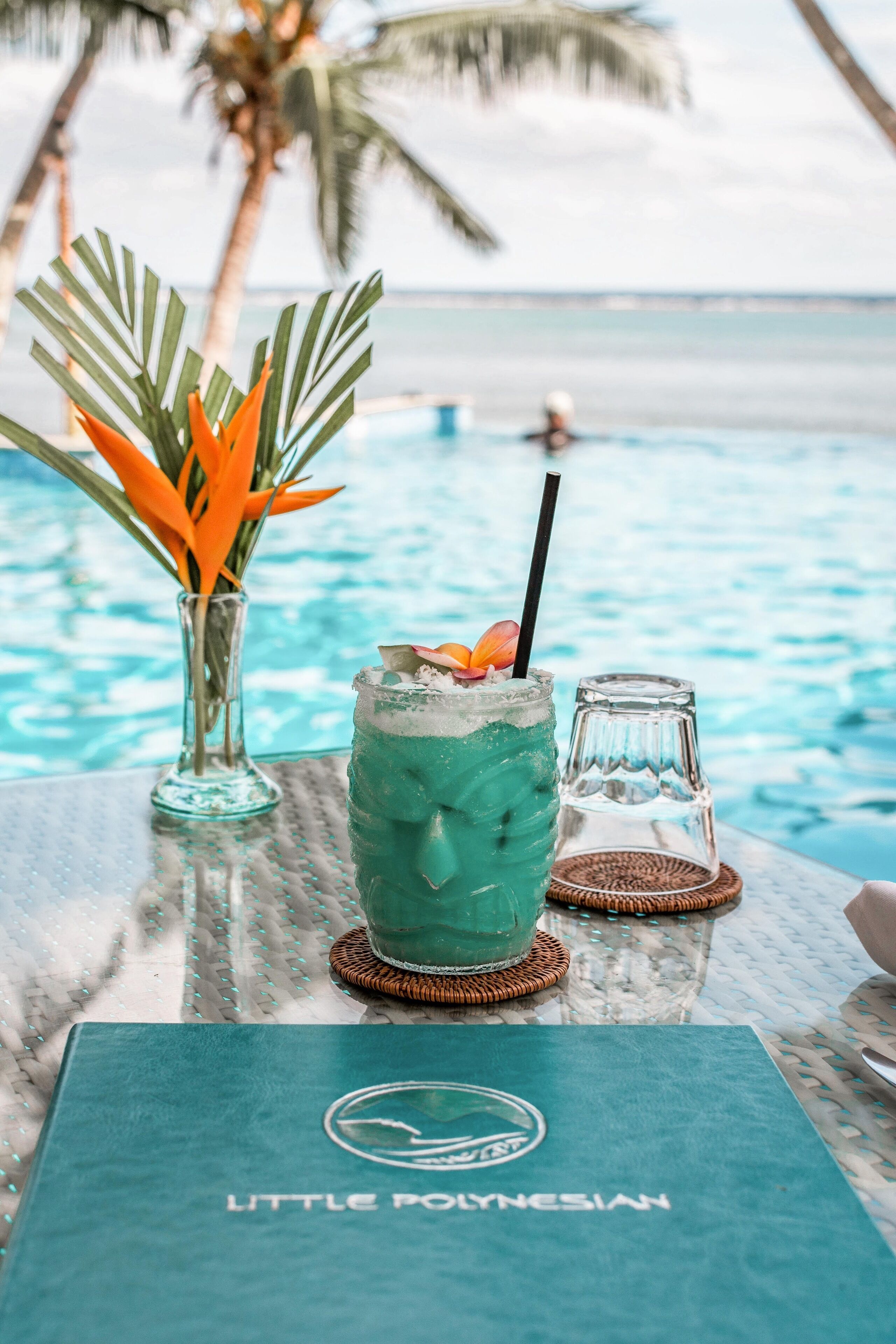 A table with a drink, a glass vase with flowers, and a menu at a poolside location.