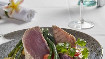 A dining table with a plate of food, a glass of white wine, and a napkin with a flower.