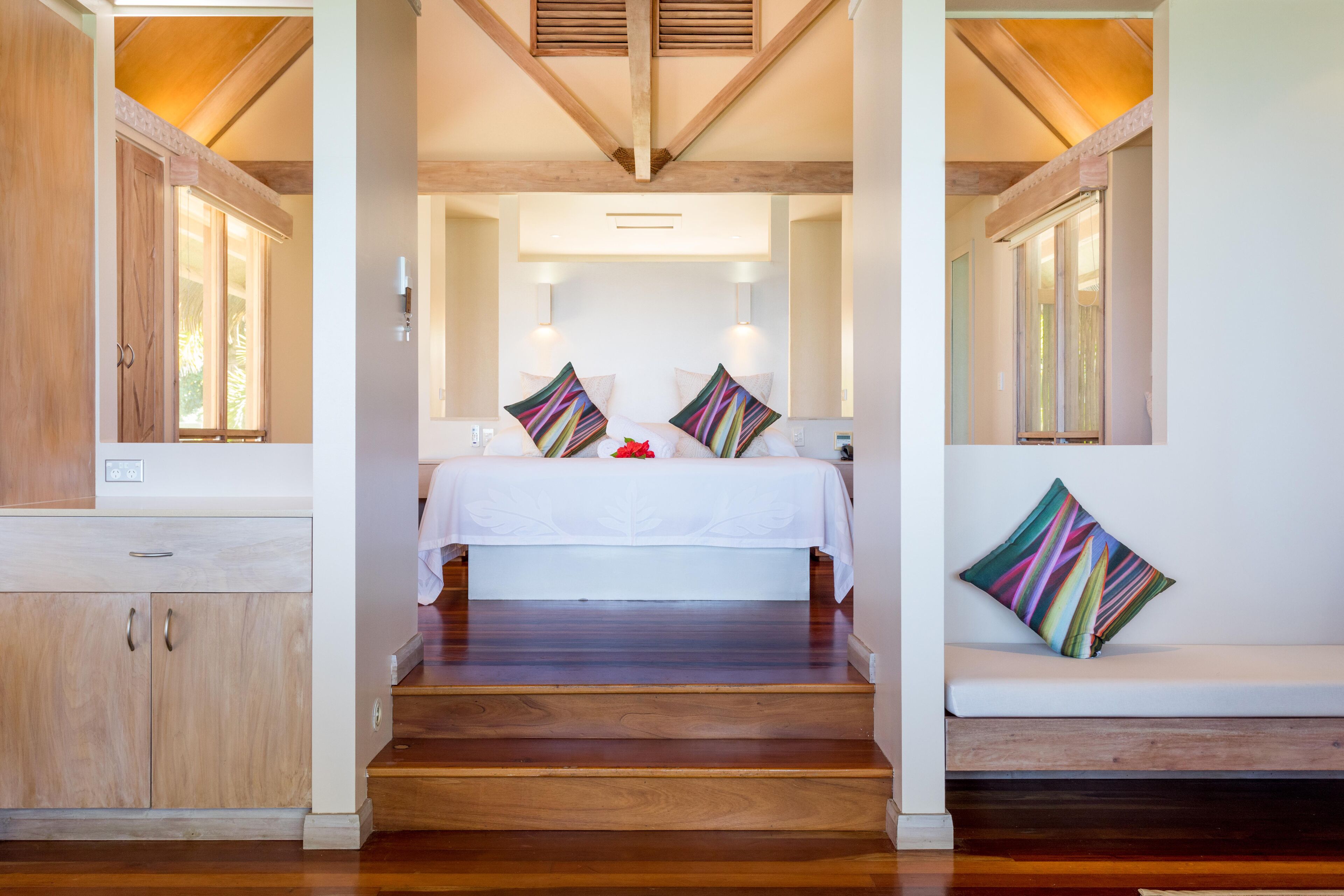 A bedroom with a wooden floor, a bed with white bedding, two wall-mounted lights, and a window with blinds.