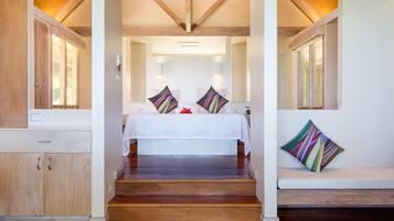 Un dormitorio con suelo de madera, cama con ropa de cama blanca, dos luces empotradas en la pared y una ventana con persianas.